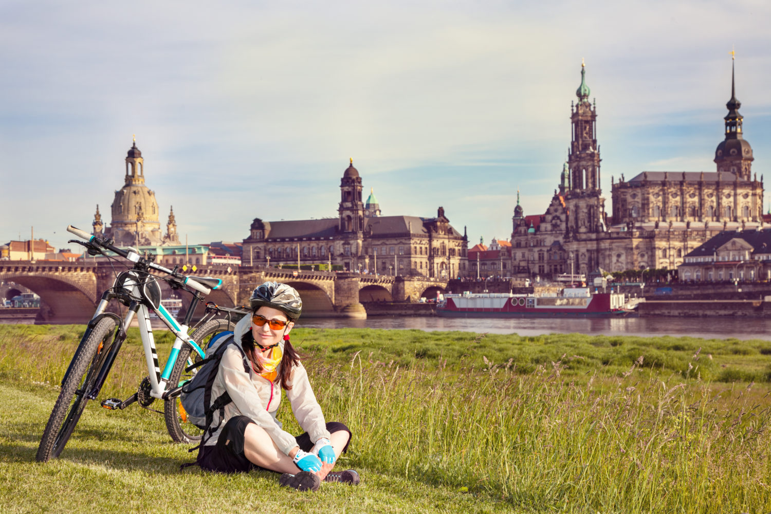 Female cyclist sitting on grass and resting with Old Town of Dresden, Germany in the background