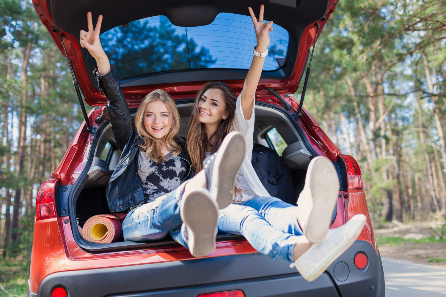 Two happy young women sitting in a parked car boot while car sharing from Prague to Leipzig