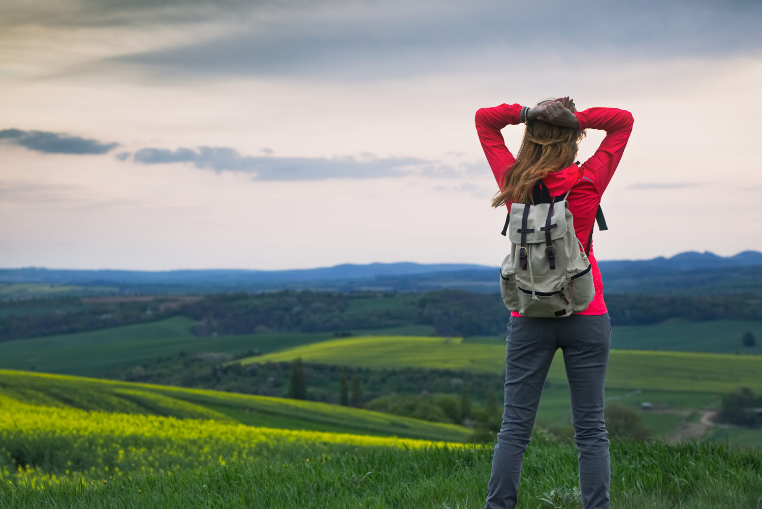 Young woman in red blazer with gray backpack looking at a view of Czech countryside while walking from Prague to Dresden