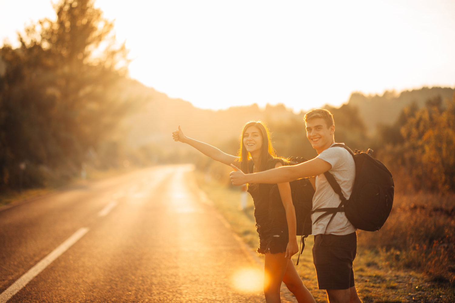 Young man and woman hitch-hiking on a countryside road