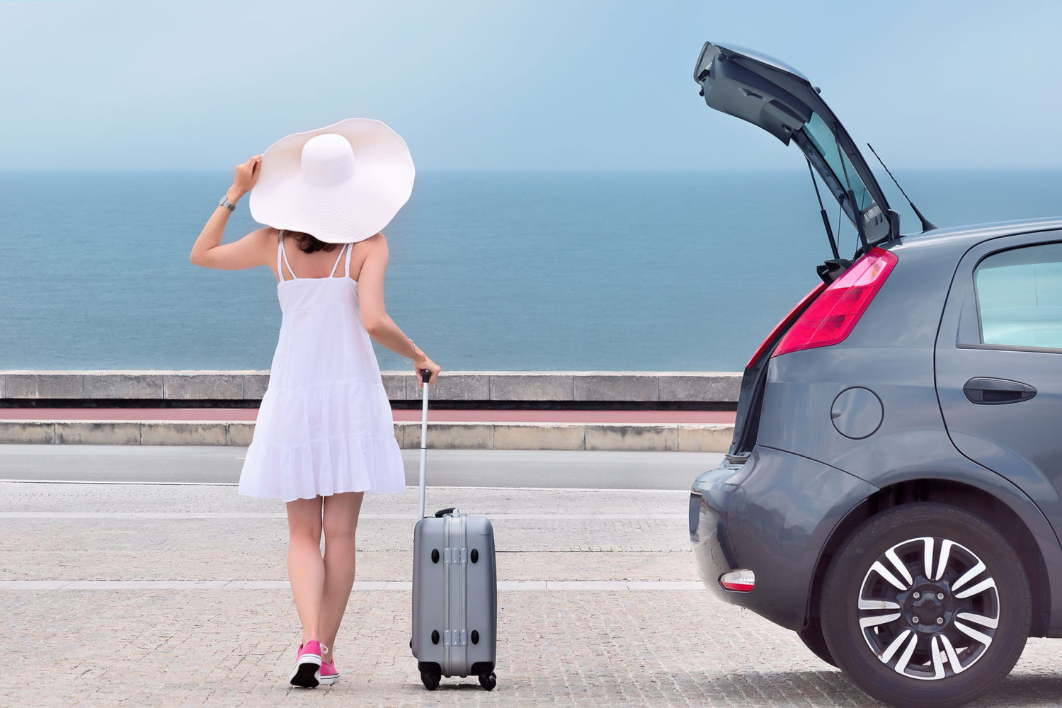 Woman in a big white hat walking towards a private hire car with her luggage